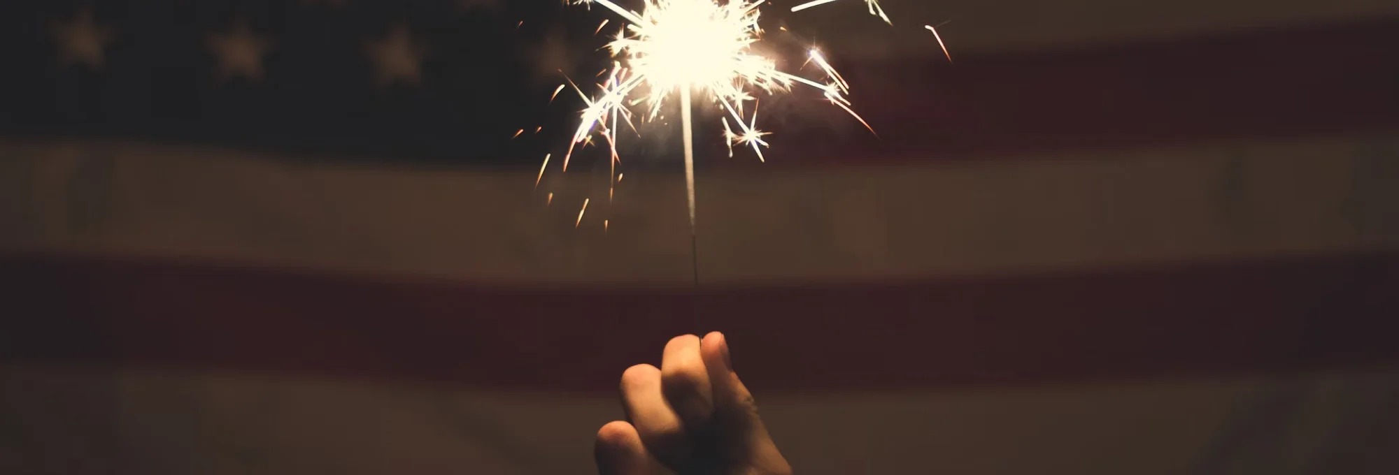 Hand holding sparkler in front of American flag